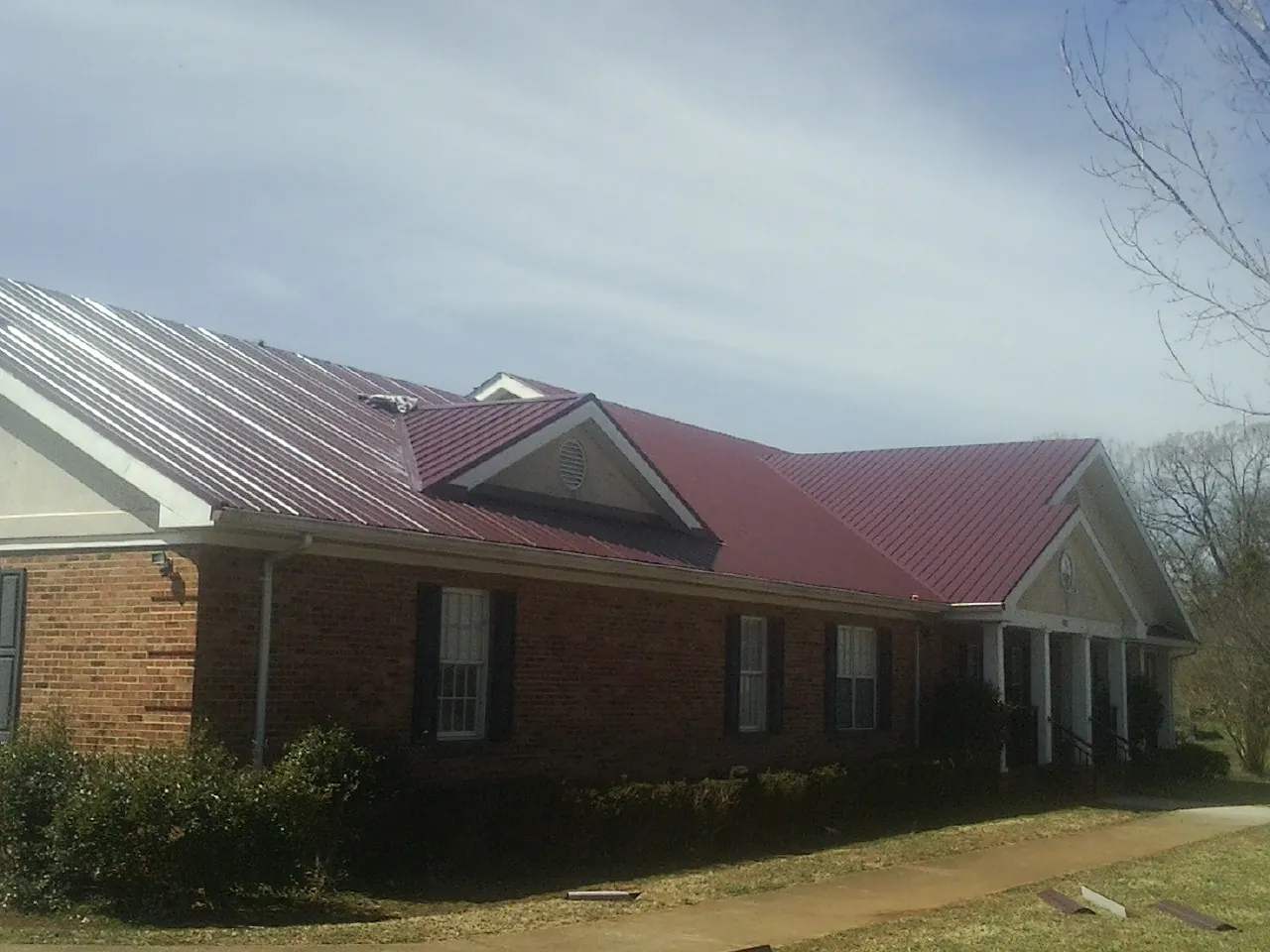 Red metal roof with gabled entries on a long brick building, from a Hail Damage Roof Repair job in Orrville