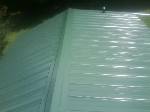 New green metal panels meeting at the ridge of a roof — Flat Roof Repair work by our crew in Orrville