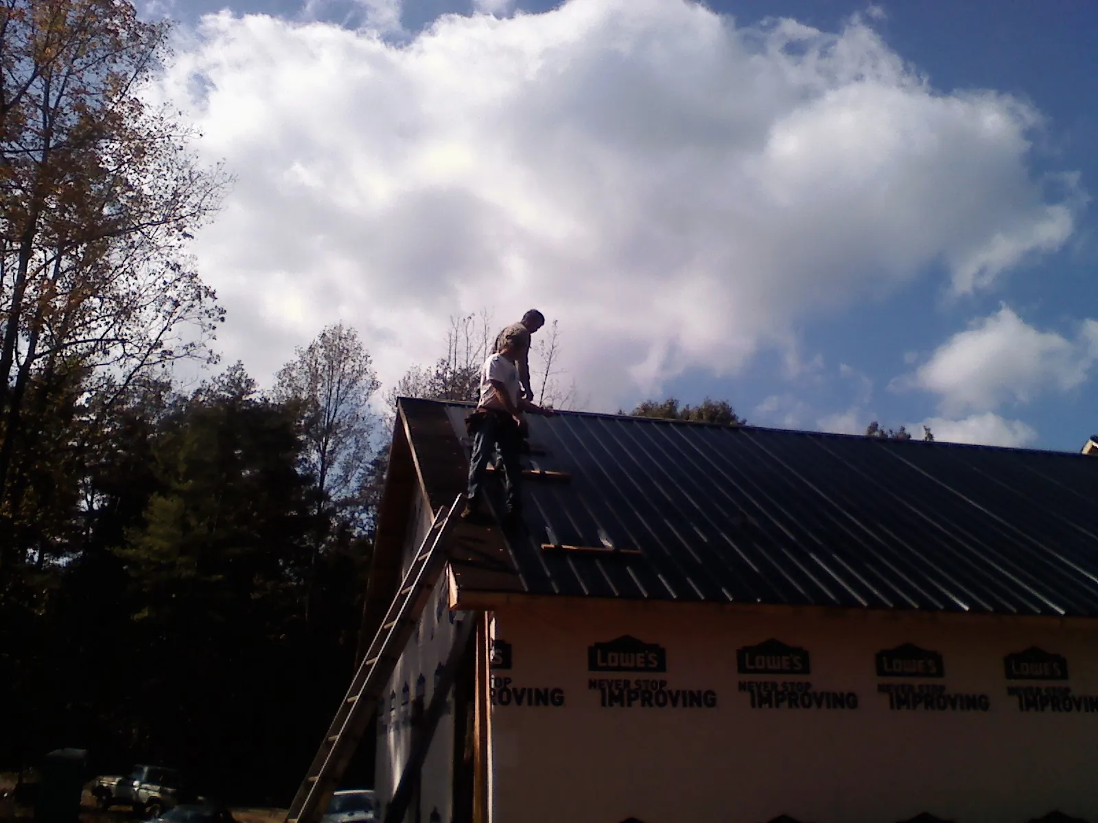 Roofer fastening dark metal panels high against a cloudy sky, from a Roof Inspection job in Orrville