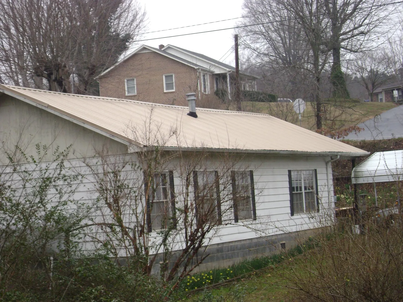 Tan metal roof on a white sided house set into a hillside — Commercial Roofing by Roofing Brothers in Orrville