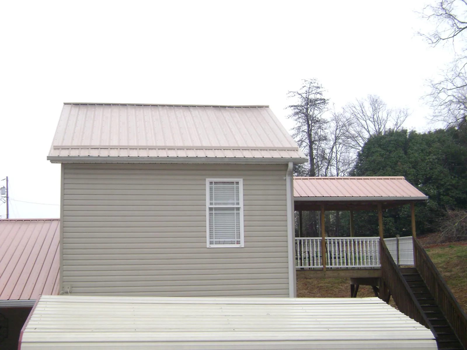 Tan metal roofs on a two story addition and attached porch, from a Roof Replacement job in Orrville